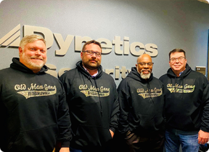 Four men wearing black sweatshirts standing in front of a wall.