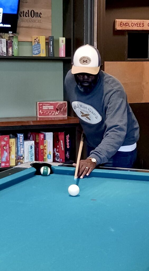 A man playing pool with his hat on.