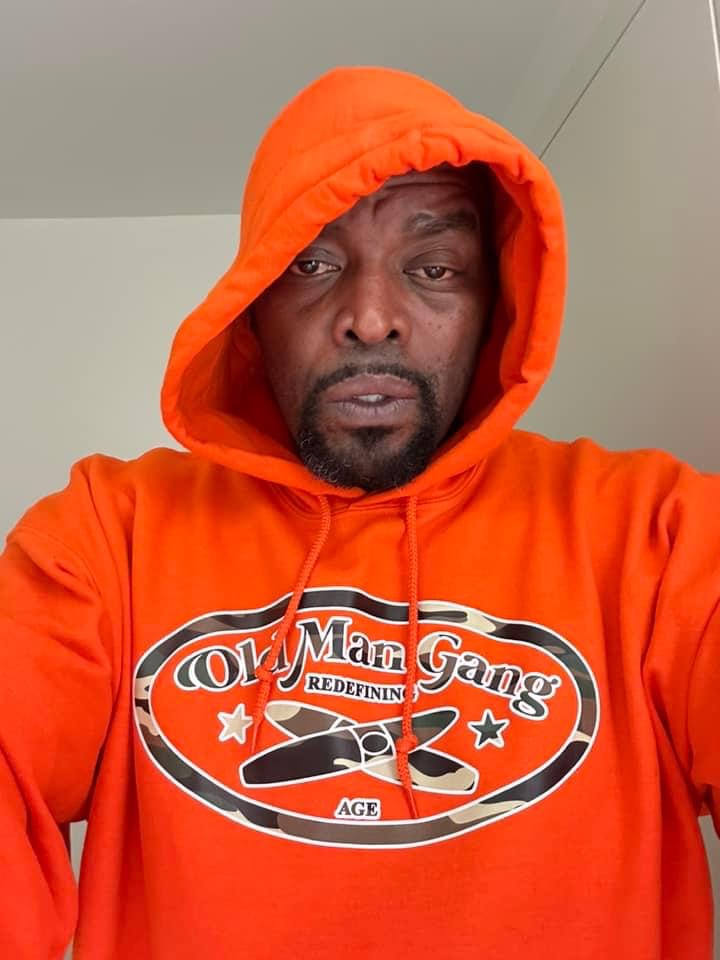 A man in an orange hoodie with the words " old mac gang " on it.