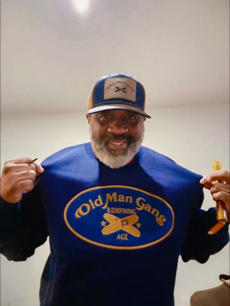 A man wearing an old man gang shirt and hat.